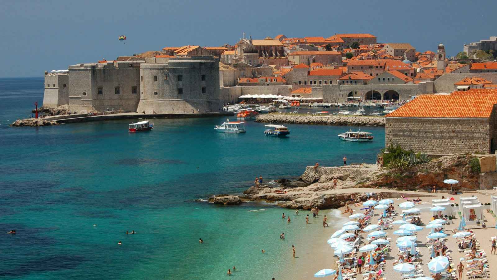 A landscape shot of Dubrovnik's old town with a beach full of people in the foreground.