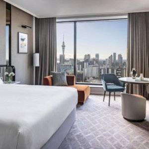 An airy white hotel room at the Cordis in Auckland with a view of the city skyline from the huge window.