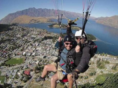 Gay couple using taking a photo with a selfie stick as they paraglide over Queenstown in New Zealand.